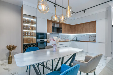 A kitchen with a beautiful interior design. White kitchen set, stylish ceiling lights, .vases with flowers.