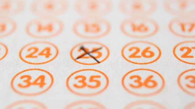 A man marks with a pen numbers 25, 46, 44, 67, 75 on a lottery ticket. The rows of orange numbers in orange circumferences on the white ticket are arranged horizontally. Close-up horizontal video