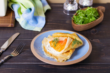 Wrapped thin pancake with filling - smoked salmon and cream cheese and pancake with scrambled egg and salmon. Crepes on blue plates
