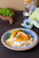 Wrapped thin pancake with filling - smoked salmon and cream cheese and pancake with scrambled egg and salmon. Crepes on blue plates