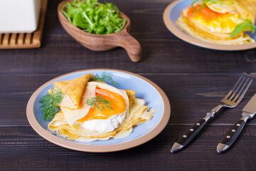 Wrapped thin pancake with filling - smoked salmon and cream cheese and pancake with scrambled egg and salmon. Crepes on blue plates