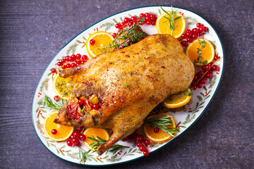 Roasted duck served with oranges and red currants on white plate on dark background. View from above, top view