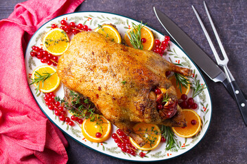 Roasted duck served with oranges and red currants on white plate on dark background. View from above, top view