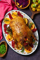 Roasted duck served with oranges and red currants on white plate on dark background. View from above, top view