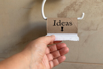 una mano tomando la ultima toalla de papel higiénico, el rollo de cartón vacío con la palabra "Ideas" y una flecha apuntando hacia abajo a la última hoja de papel