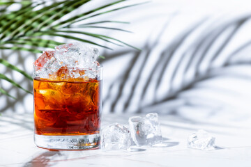 The Bottom Line alcoholic cocktail drink with scotch whiskey, sherry, liqueur and bitters. White marble table with palm leaves and shadows