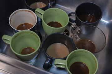 Cups with coffee remnants in various shades of brown await their turn for cleaning, emphasizing a dependency on the invigorating beverage. 