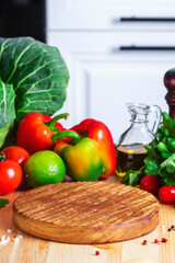 Food cooking background with round wood board, vegetables, herbs, olive oil, spice grinder, modern classic white kitchen