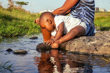 Fototapeta premium A beautiful young African woman playing outdoors with her baby boy at sunset