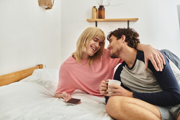 Obraz premium Two men share a warm smile in bed with drinks, highlighting their love and bond.