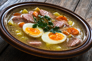 Sour rye soup with sausages and boiled eggs on wooden table. Traditional Polish soup for Easter