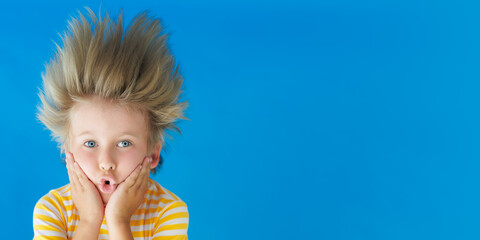 Funny kid with his hair standing on end. Surprised child on a blue background with copyspace. Summer vacation concept