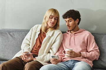Two men share a tender moment on a couch, engaging with a mobile device while sipping drinks.