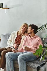 Obraz premium Two men sit together on a couch, sharing drinks and smiles in a warm, inviting space.