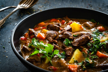 Beef stew with vegetables and potatoes on black table