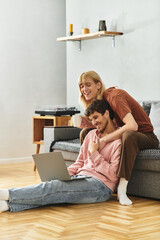 Two joyful men relax on a couch, laughing and sharing a moment as they use their laptop.