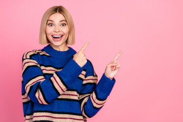 Cheerful young woman in a bright sweater pointing excitedly against a pink background