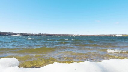 A peaceful winter scene at Lake Ronkonkoma, Long Island. Clear blue skies reflect over shimmering icy waters, creating a tranquil moment of natural beauty. Captures the serene charm of the season.