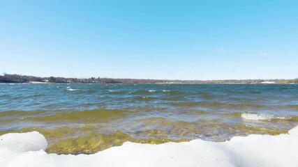 A peaceful winter scene at Lake Ronkonkoma, Long Island. Clear blue skies reflect over shimmering icy waters, creating a tranquil moment of natural beauty. Captures the serene charm of the season.