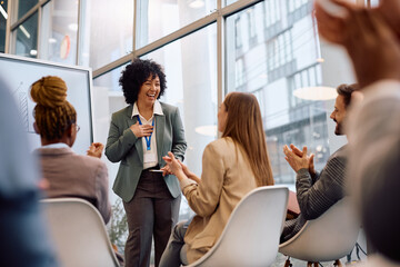 Happy business seminar speaker receiving applause from her colleagues in board room.