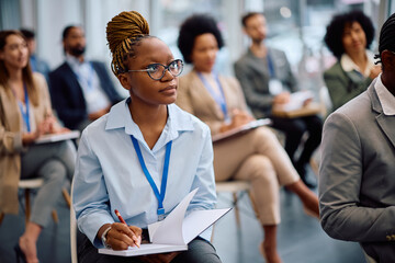 Young black businesswoman taking notes while attending education event in board room.