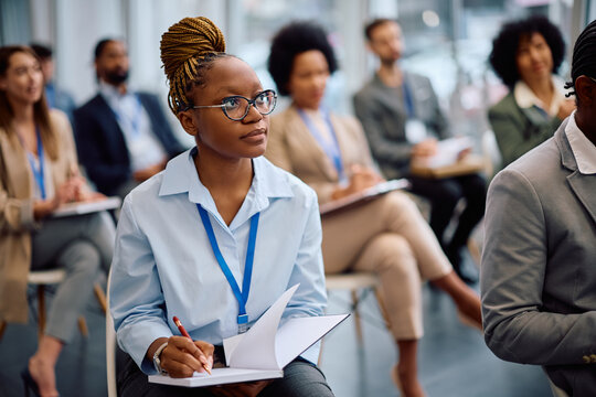 Young black businesswoman taking notes while attending education event in board room.