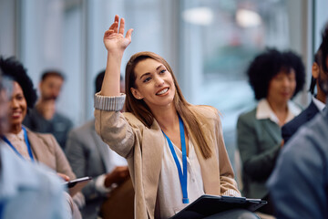 Happy entrepreneur raising her arm to ask question during business conference in board room.