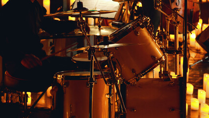 Close-up of a drum kit being played on a dimly lit stage surrounded by candles.