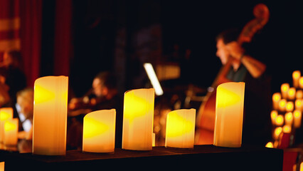 A close-up of a row of lit candles in front of a blurred background of a musical performance. Candlelight concert.