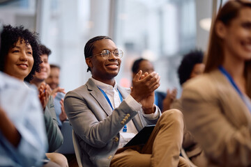 Happy black businessman applauding on education event at conference hall.