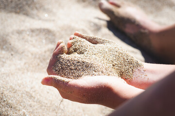 Hand releasing dropping sand. Fine Sand flowing pouring through fingers against black background....