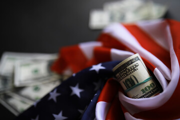 Roll of Dollar Bills Wrapped in American Flag with Scattered Cash Background