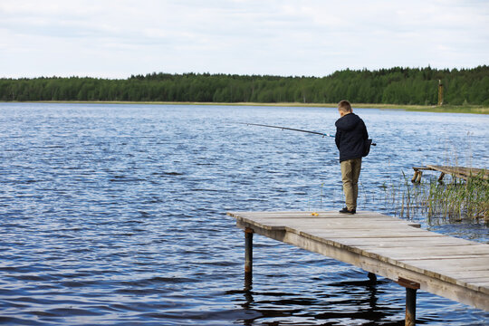 Boy Fishing Alone on Wooden Dock by Calm Lake on a Cloudy Day