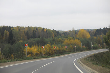 Scenic Curved Road Through Autumn Forest with Safety Signs and Overcast Sky