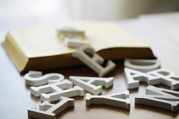 Wooden Alphabet Letters on Table with Open Book in Soft Focus Background © alexkich