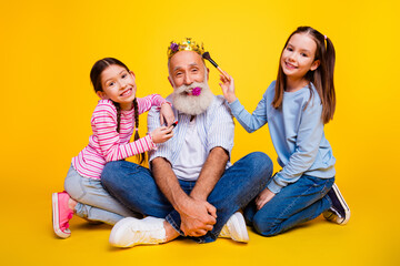 Grandfather bonding with his two granddaughters in cheerful playful scene, surrounded by bright yellow background.