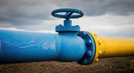 Blue and yellow industrial gas pipeline valve against a cloudy sky