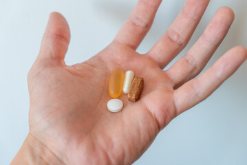 Close up of open hand holding various vitamins such as fish oil and other capsules and pills and round tablets on light background