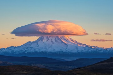 Fototapeta premium Majestic snow-capped mountain peak at sunset, dramatically capped by a lenticular cloud.