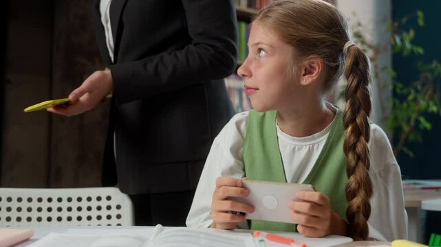 Caucasian little girl teen child kid schoolgirl school bad behavior student pupil playing mobile phone game gadget addiction distract from studying strict teacher professor takes away cellphone indoor