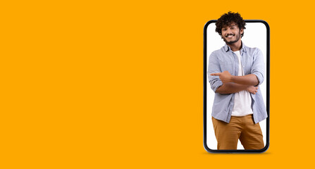 A cheerful young man smiles and poses with crossed arms while appearing to interact with a large smartphone screen in a vibrant yellow background. The scene focuses on modern communication.