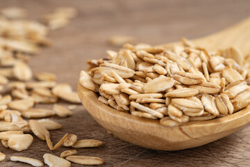 Close-up of raw rolled oats in a wooden spoon on a rustic wooden surface, perfect for healthy eating, natural food, and cooking concepts.