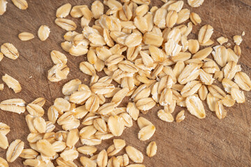 Scattered raw rolled oats on a rustic wooden surface. Ideal for healthy eating, organic food, diet concepts, and natural cooking backgrounds.