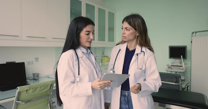 Two young Hispanic female doctors talking in ultrasound scanning office, using digital tablet, discussing ultrasound scanning medial research, medical technology, checkup electronic result