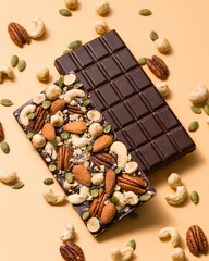 Two dark chocolate bars with mix nuts on beige background. Confectionery. Demonstration of sides of handmade chocolate bars. Cashews, hazelnuts, almonds, pecan, pumpkin seeds. Sweet food concept.