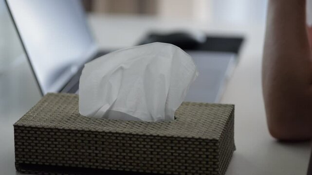 Hand pulling tissue near laptop workspace