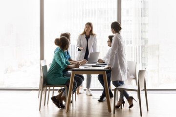In modern skyscraper conference room, five multinational clinic staff solve current issues, review...