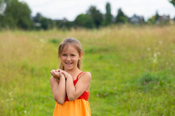 Fototapeta premium portrait of a little girl in a bright rainbow-colored sundress on a field in summer. child's emotions.