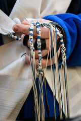 Closeup of the hand of an Orthodox, Jewish man holding blue techelet and white tzitzit strings...