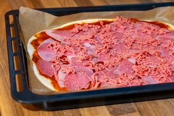 Delicious homemade pizza preparation with various meats and a rich tomato base on a baking tray